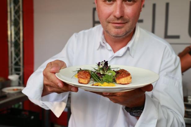 Ein Koch präsentiert ein Gericht mit zwei kleinen Küchlein und Salat auf einem weißen Teller.