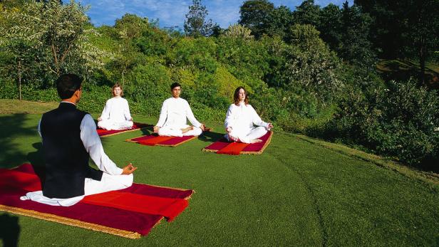 Eine Gruppe von Menschen meditiert auf roten Matten im Freien.