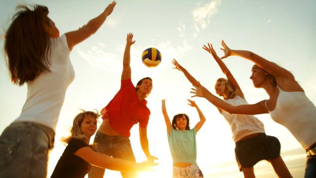 Eine Gruppe junger Leute spielt Beachvolleyball bei Sonnenuntergang.
