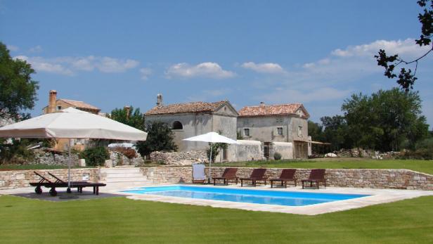 Ein Swimmingpool mit Liegestühlen vor einem alten Gebäude unter blauem Himmel.