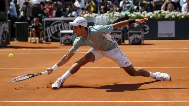 Ein Tennisspieler schlägt einen Ball auf einem Sandplatz.