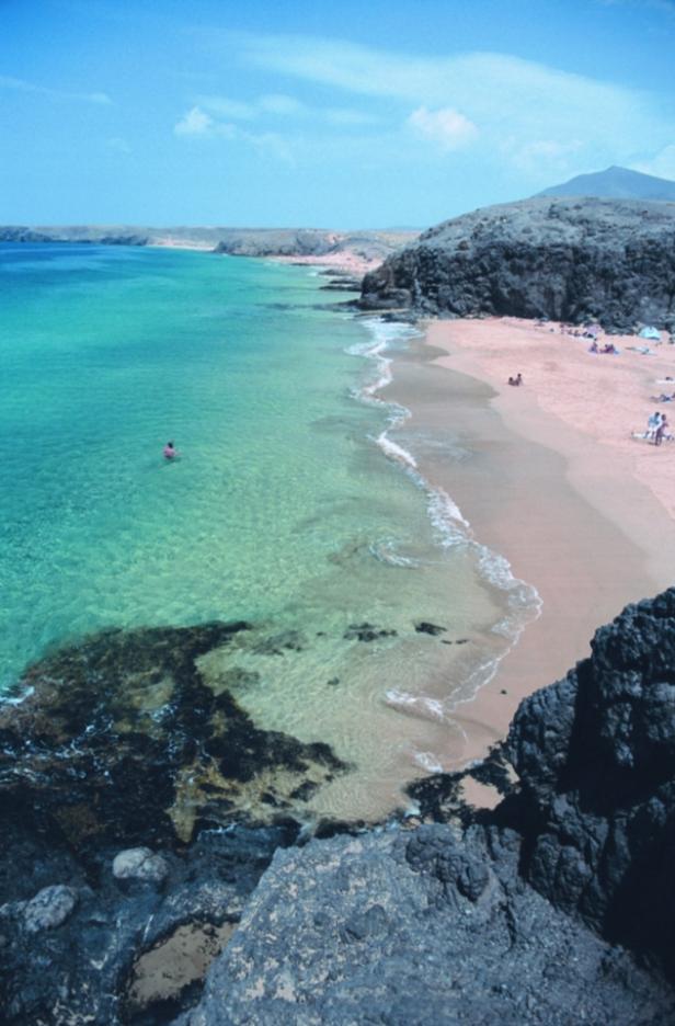 Ein Strand mit türkisfarbenem Wasser und hellrosa Sand lädt zum Baden ein.