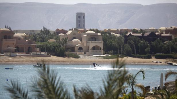 Eine Person benutzt ein Flyboard auf dem Wasser vor einer Küstenstadt.