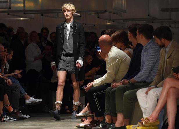 Ein Mann mit blonden Haaren läuft auf einer Modenschau vor Publikum.