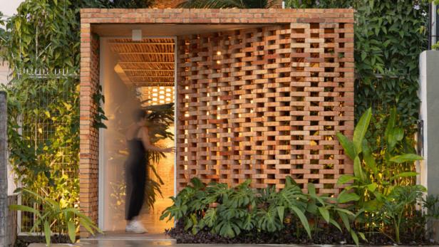 Eine Frau betritt ein Gebäude mit einer Fassade aus roten Ziegelsteinen und tropischer Vegetation.