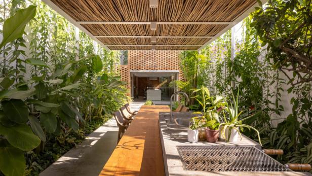 Ein Außenbereich mit Grill, Spüle, Tisch und üppiger tropischer Bepflanzung.