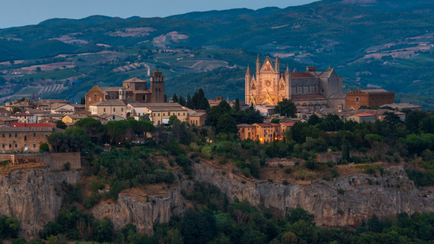 Die Stadt Orvieto in Umbrien mit dem beleuchteten Dom auf einem Hügel.