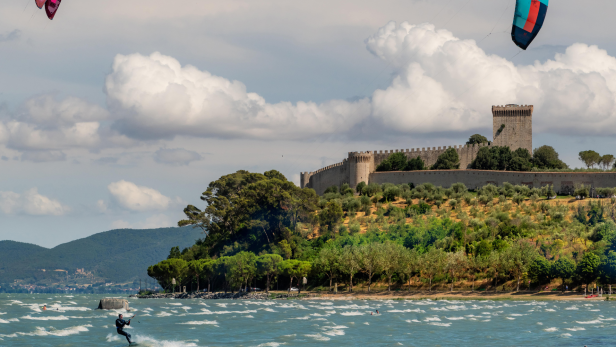 Ein Kitesurfer auf dem Trasimenischen See vor der Kulisse einer mittelalterlichen Burg.