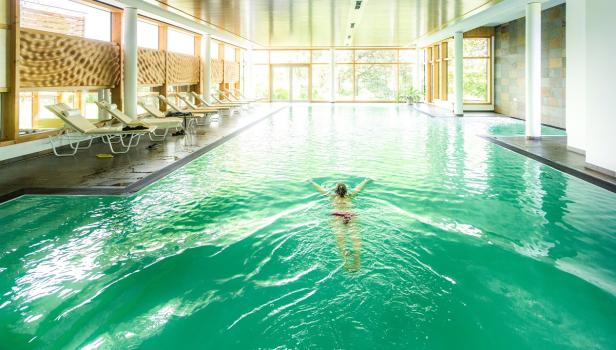 Eine Frau schwimmt in einem hellen Hallenbad mit türkisfarbenem Wasser.