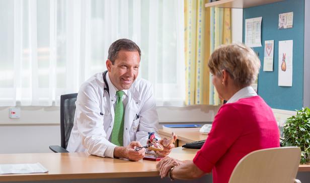 Ein Arzt erklärt einer Patientin ein Herzmodell in seiner Praxis.