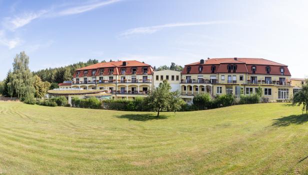 Ein gelbes Hotelgebäude mit roten Dächern und einem gepflegten Rasen davor.