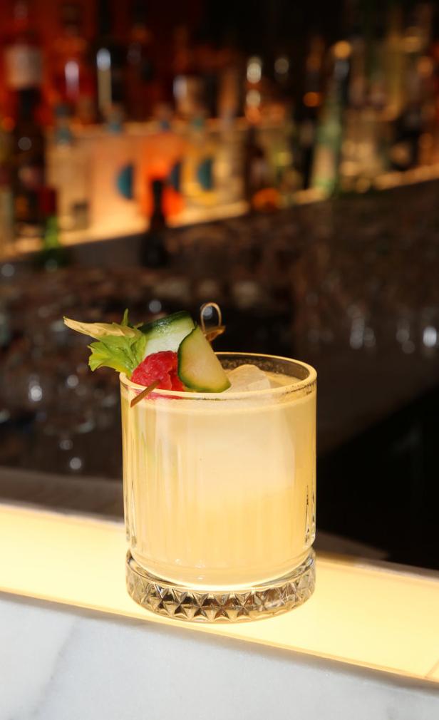 Ein Cocktail mit Eiswürfeln, Gurke, Sellerie und Himbeere an einer Bar.
