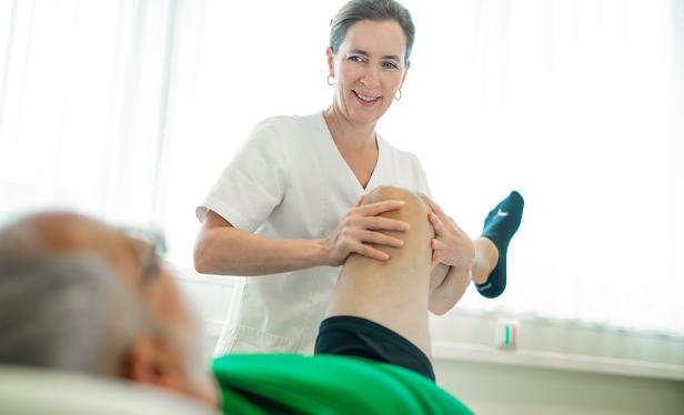 Eine Physiotherapeutin behandelt das Knie eines Patienten.