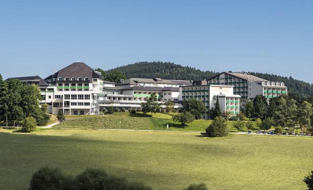Ein großes, weißes Gebäude mit grünen Akzenten liegt in einer grünen Landschaft.