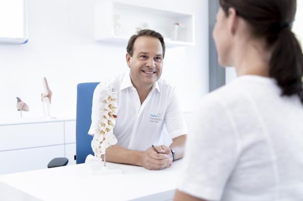 Ein Arzt im weißen Kittel erklärt einer Patientin etwas anhand eines Wirbelsäulenmodells.