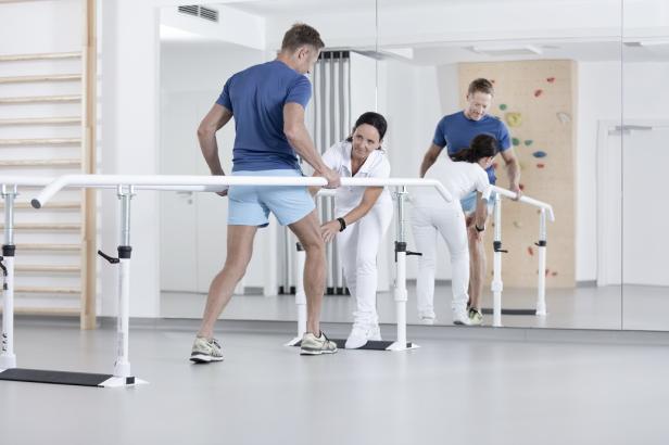 Ein Physiotherapeut unterstützt einen Mann bei Gehübungen an einem Barren.