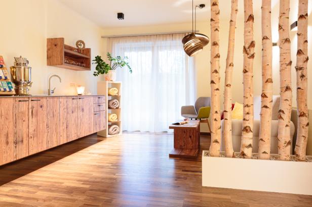 Ein heller Raum mit Holzboden, einer Küchenzeile und Birkenstämmen als Raumteiler.