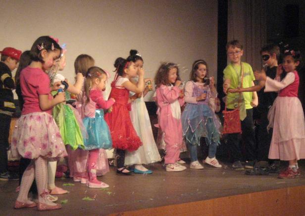 Eine Gruppe Kinder in Kostümen steht auf einer Bühne und pustet Seifenblasen.