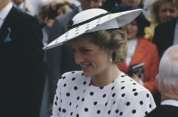 Prinzessin Diana lächelt in einem weißen Kleid mit schwarzen Punkten und einem passenden Hut.