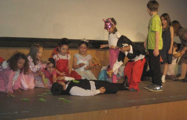 Kinder führen ein Theaterstück auf, in dem ein Junge als Toter auf der Bühne liegt.