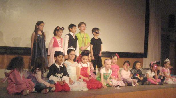 Eine Gruppe von Kindern in Kostümen sitzt auf einer Bühne.