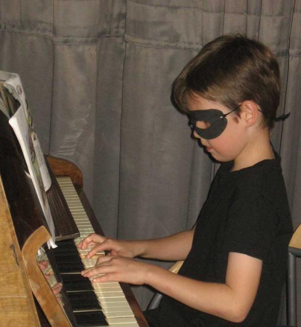 Ein Junge mit einer schwarzen Maske spielt Klavier.