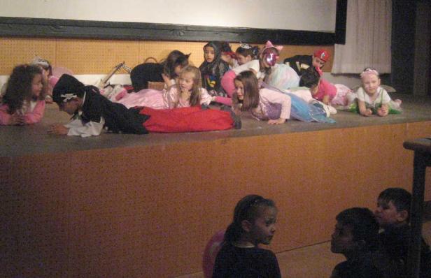 Eine Gruppe Kinder in Kostümen liegt auf einer Bühne.