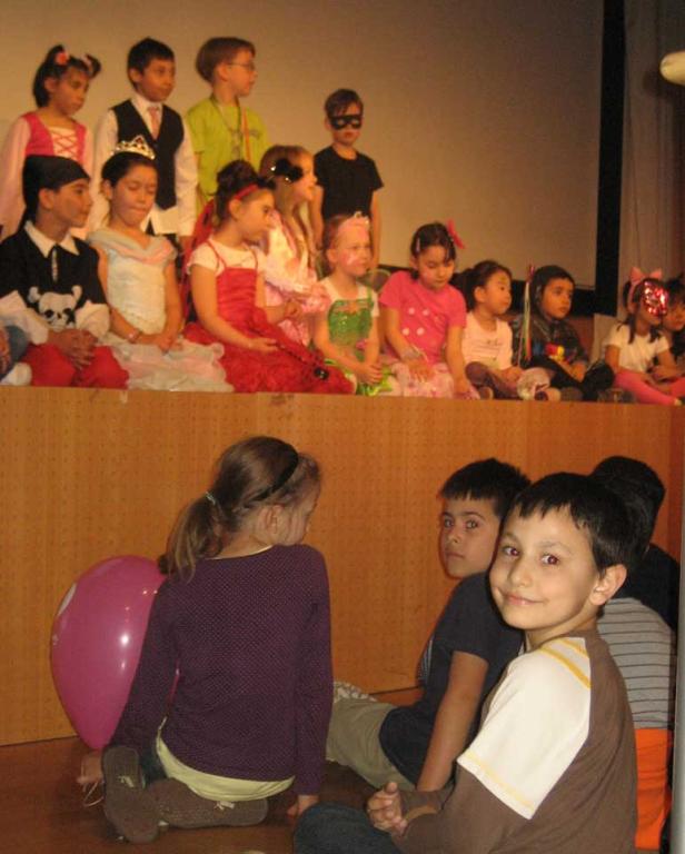 Eine Gruppe von Kindern in Kostümen sitzt auf einer Bühne.