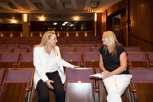 Zwei Frauen sitzen in einem leeren Theatersaal und unterhalten sich.
