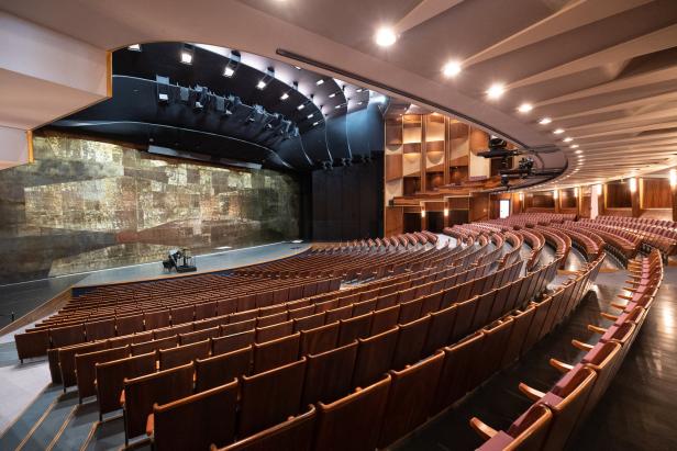 Blick in einen leeren Theatersaal mit Bühne und vielen Sitzplätzen.