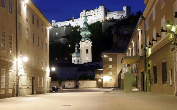 Blick auf die Festung Hohensalzburg und die Kajetanerkirche bei Nacht.