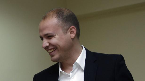 Ein lächelnder Mann im Anzug vor einem hellen Hintergrund.