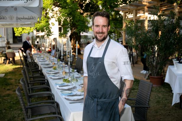 Ein Koch steht vor einer langen, festlich gedeckten Tafel im Freien.