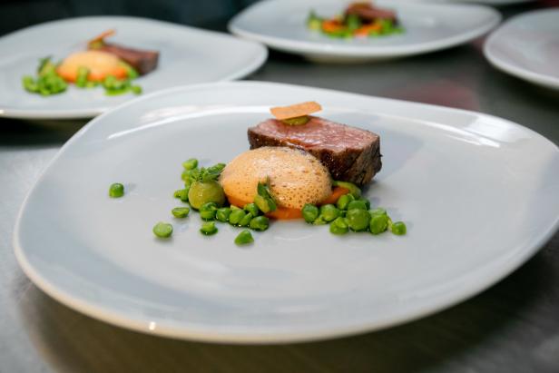 Ein Teller mit einem Stück Fleisch, Erbsen und einer hellen Soße.