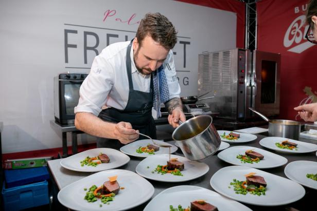 Ein Koch garniert Tellern mit Fleisch, Erbsen und Karotten mit Soße.