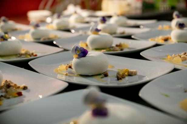 Viele Teller mit weißen Desserts, garniert mit Blüten und Krümeln.