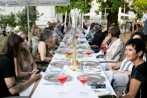 Gäste sitzen an einer langen, festlich gedeckten Tafel im Freien.