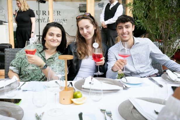 Drei Personen sitzen an einem Tisch und halten Getränke in der Hand.