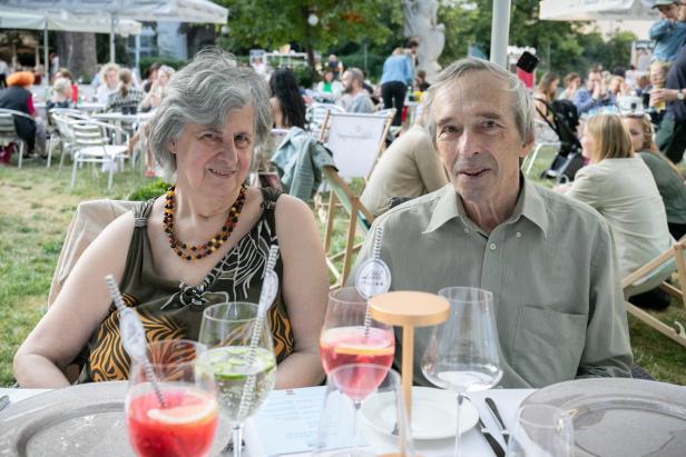Ein älteres Paar sitzt an einem Tisch im Freien mit Getränken und genießt ein Essen.