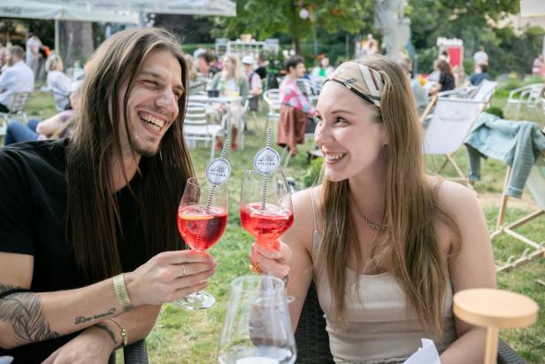 Ein Mann und eine Frau stoßen im Freien mit Aperol Spritz an.