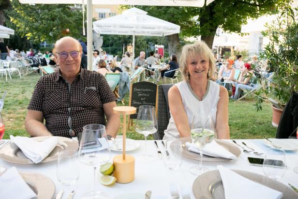 Ein Mann und eine Frau sitzen an einem gedeckten Tisch im Freien.