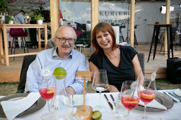 Ein Mann und eine Frau sitzen an einem Tisch mit Getränken und lächeln.