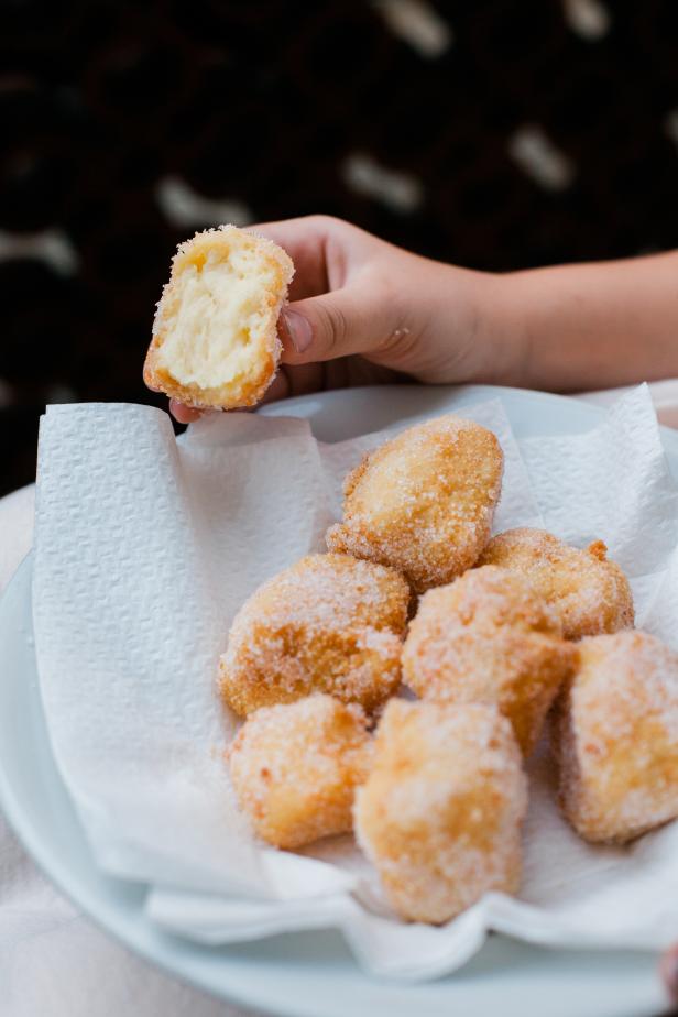 Eine Hand hält einen halbierten, zuckerbestreuten Krapfen über einem Teller mit weiteren Krapfen.