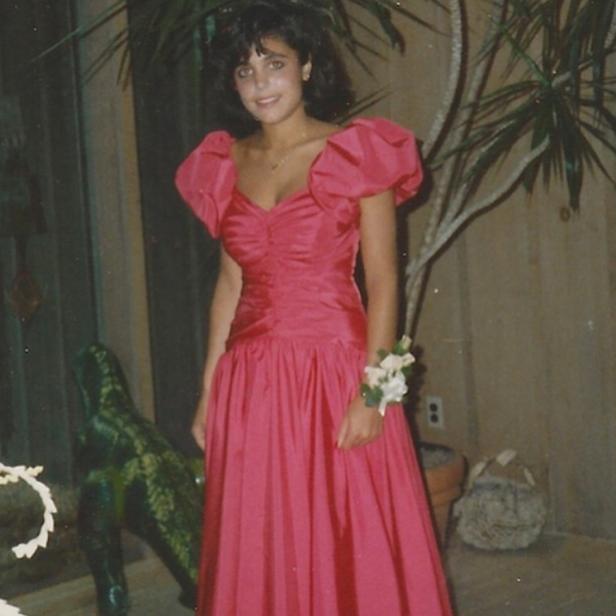 Eine junge Frau in einem roten Ballkleid mit Blumenarmband posiert für ein Foto.