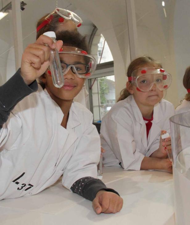 Kinder mit Schutzbrillen führen ein Experiment mit Reagenzgläsern durch.