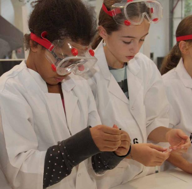Mehrere Mädchen in Laborkitteln und Schutzbrillen führen ein Experiment durch.
