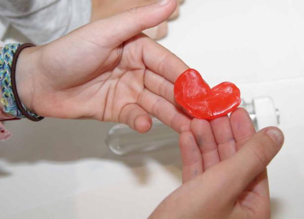 Ein Kind hält ein rotes Herz aus Knete in den Händen.