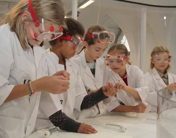 Eine Gruppe von Mädchen in Laborkitteln und Schutzbrillen führt ein Experiment durch.