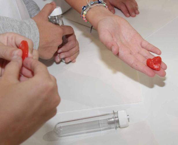 Kinderhände formen rote Herzen und füllen sie in kleine Flaschen.