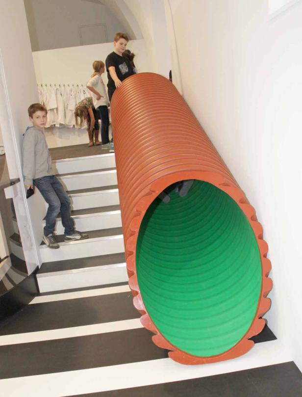 Kinder spielen mit einer großen Röhrenrutsche in einem Innenraum.